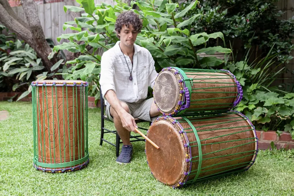 a man playing african dunun drums set in the park