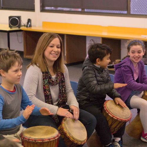 primary school teacher and a few of her students sitting and playing djembes together