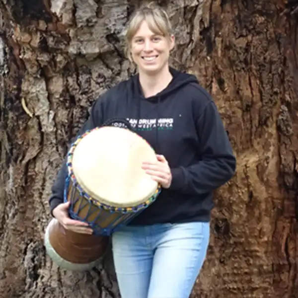 a teacher standing, holding her djembe, and smiling