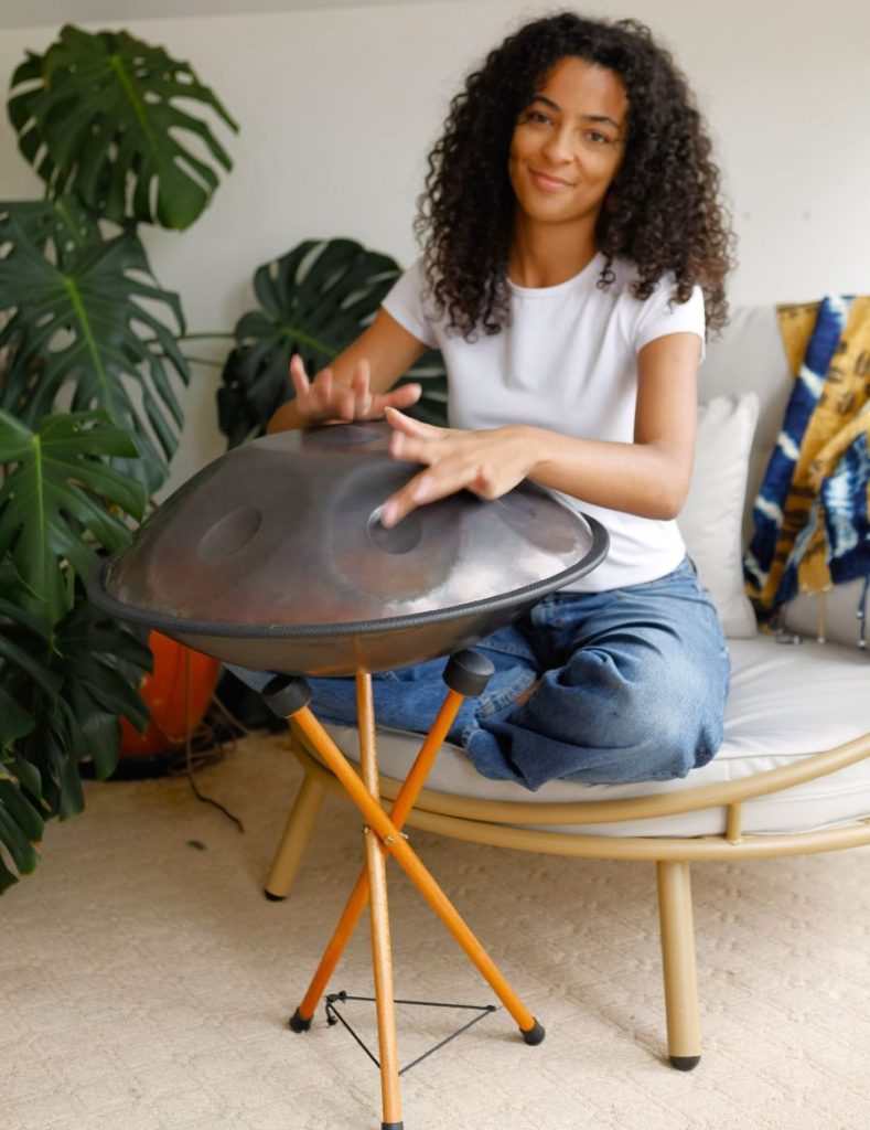 Person playing a handpan drum for sound healing in a modern indoor setting with monstera plants
