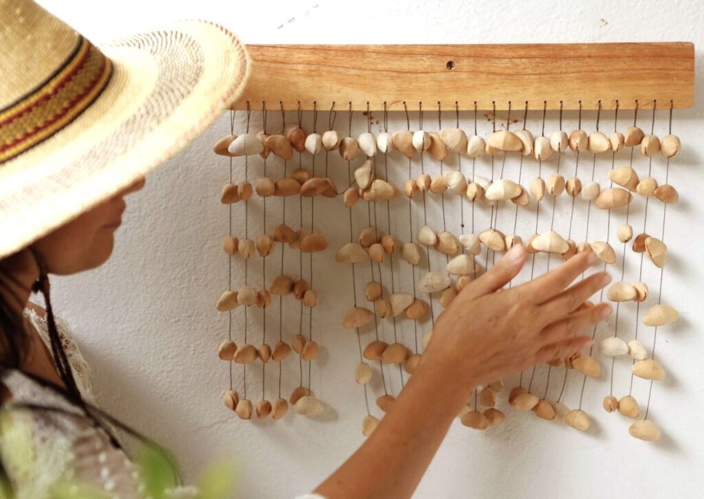 a women lightly touches seedpod chimes that are hanging on a wall