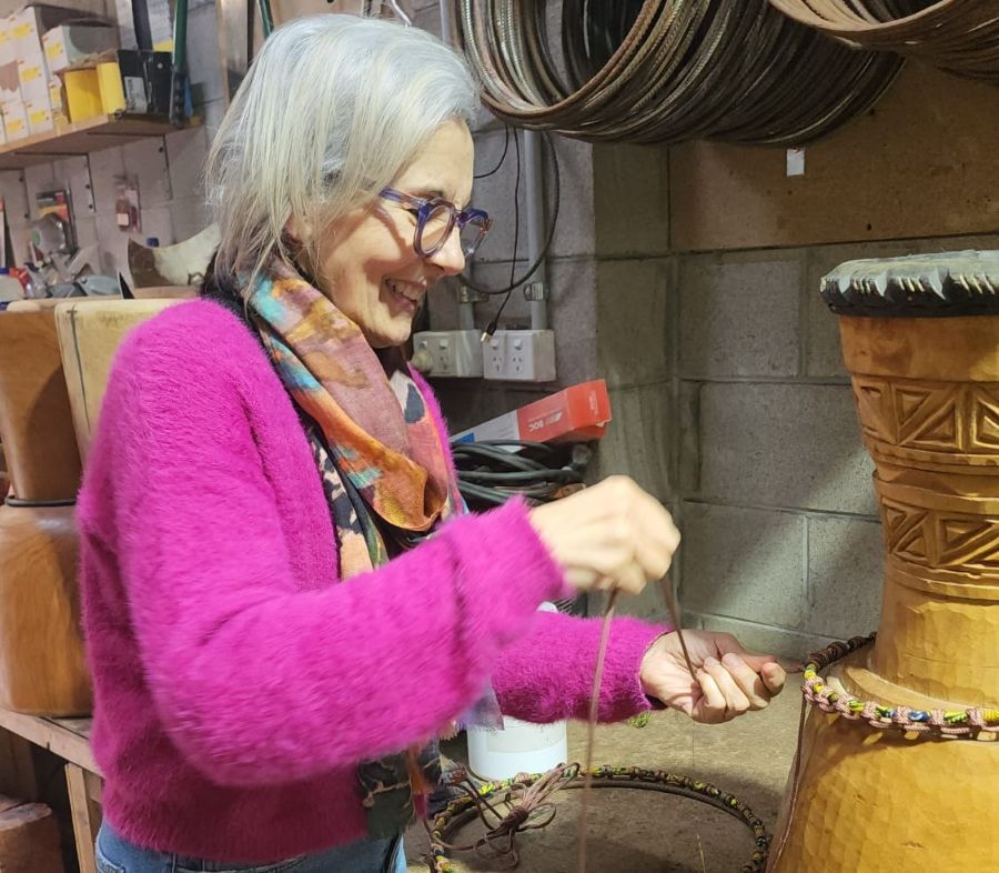 A person working on a djembe at the AD studio, showcasing the drum-making process with vibrant colors and intricate details.