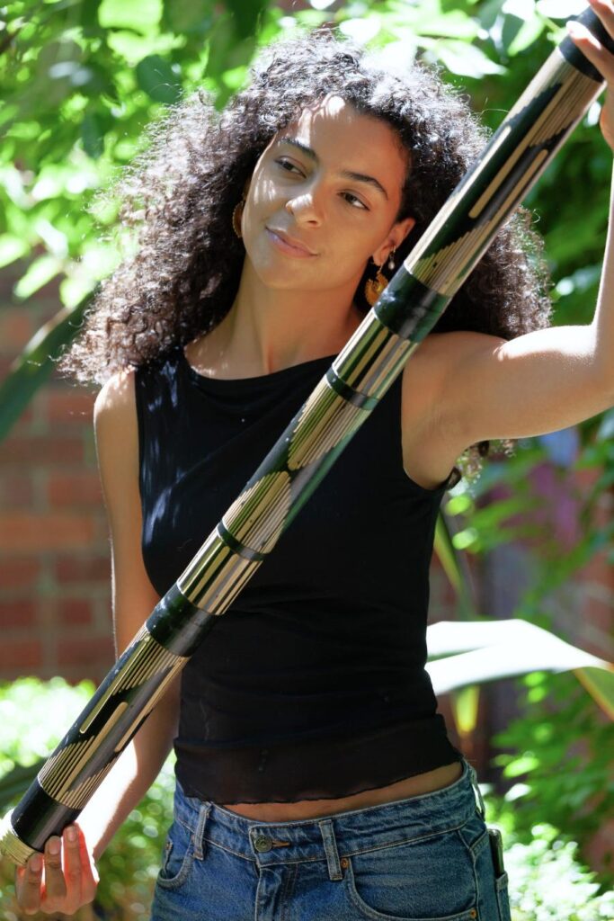 a woman holding a large rainstick made from bamboo with animal carving