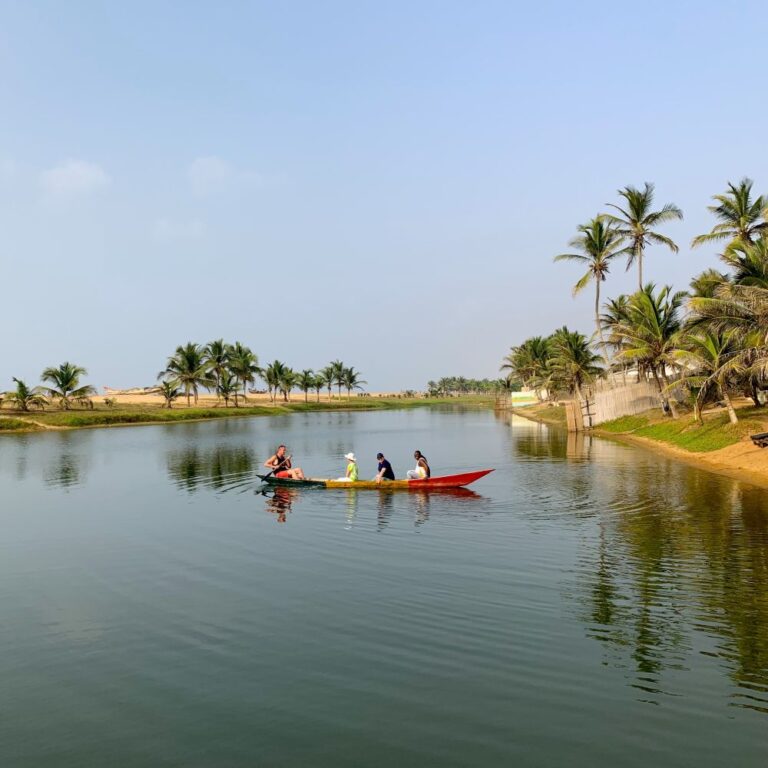 Guests enjoying a canoe ride on the serene lagoon at the Ghana retreat, surrounded by palm trees and peaceful sandy shores.