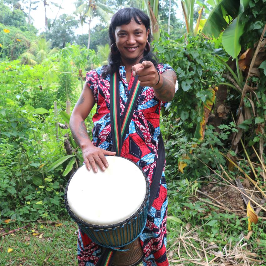 Catur playing a djembe and pointing at the camera in a tropical setting at the Bali Drum Camp