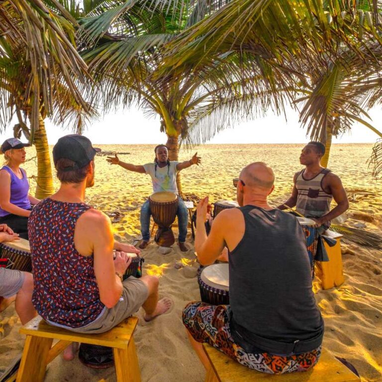 a group of people sitting on the sand playing drums