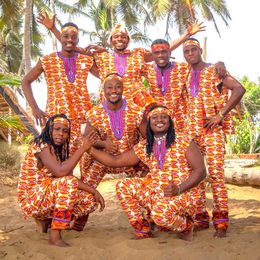 Teachers of the Rhythm Power Drumming Tour in Ghana, wearing matching vibrant traditional outfits on a tropical beach.