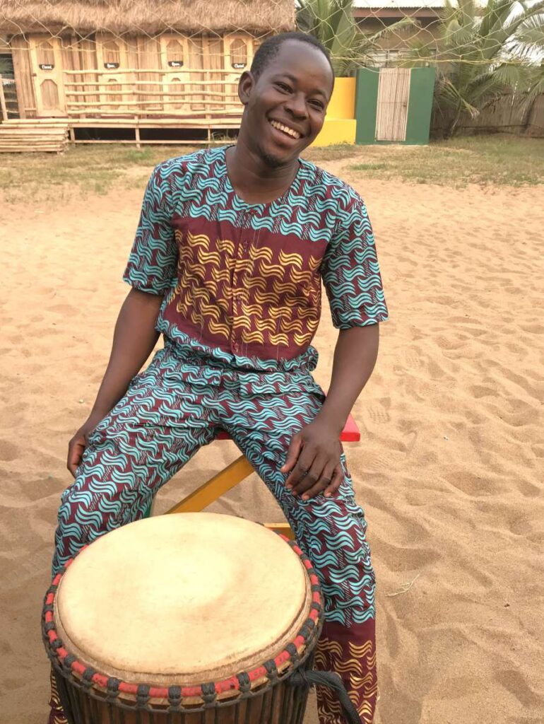 Smiling drummer sitting with a djembe in West Africa, part of the Rhythm Power Tour