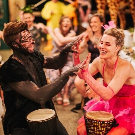 a woman and man playing djembes together and laughing at ab african drumming hens party