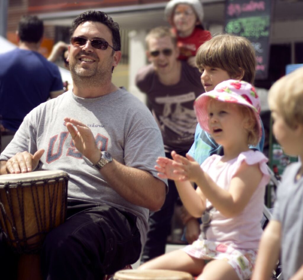 Man playing djembe with children at a community event, enjoying music and rhythm together