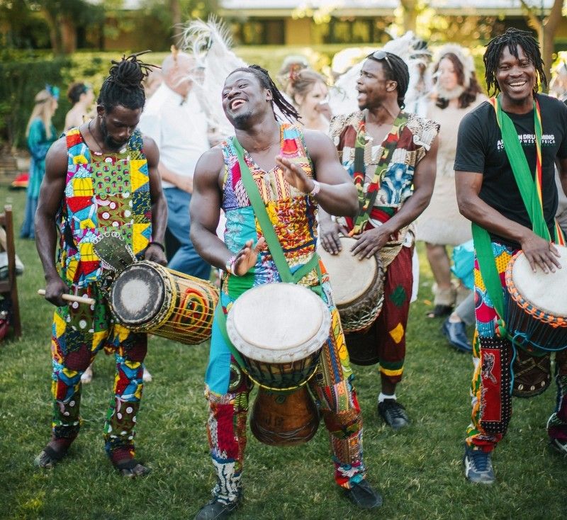 african drumming perfomers standing with a variety of drums and wearing colourful african performance clothes