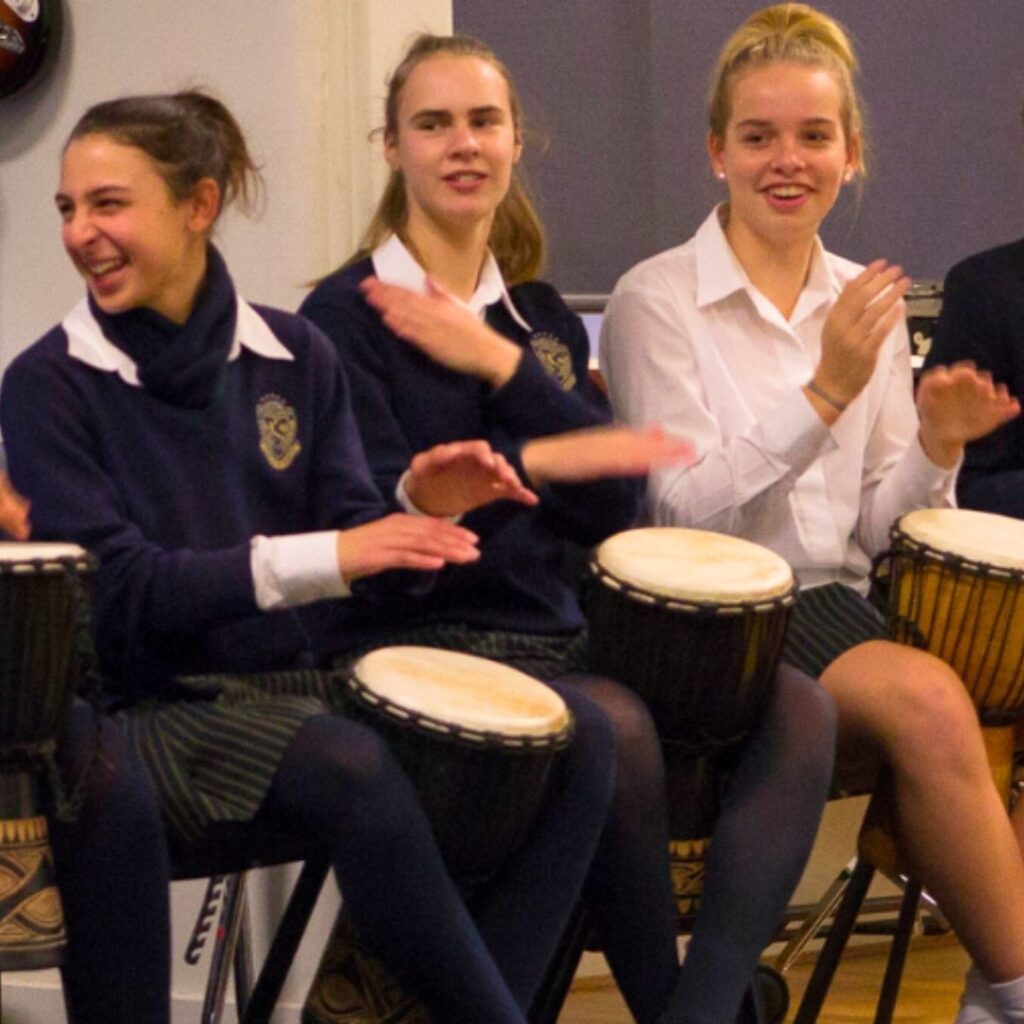 High school girls in uniform enjoying a fun drumming session with African Drumming.