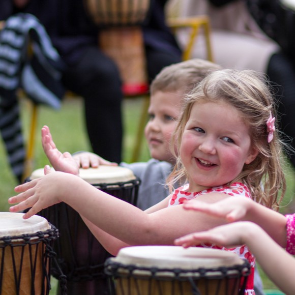 Children enjoying an African drumming workshop at a kids birthday party, smiling and playing djembes together