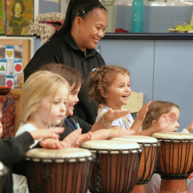 Kindergarten children clapping and playing djembes with a teacher during an African drumming incursion