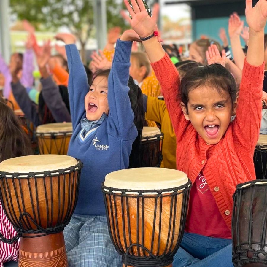 Smiling students playing djembes during a fun and engaging African Drumming school workshop