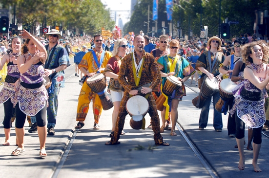 African drumming and dance group leading a street parade with djembes, movement, and vibrant costumes