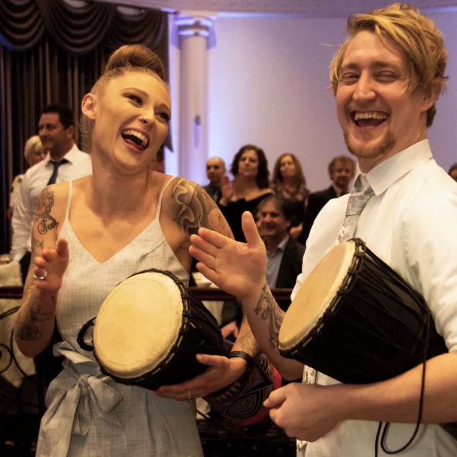 Wedding guests laughing and playing djembes together during an African drumming celebration in Australia.