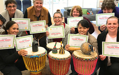 participants at the teacher training workshops standing with their certificates of completion and djembes