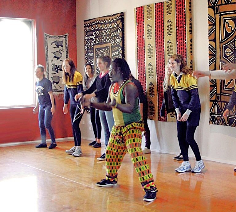 African Drumming dance workshop in the St Kilda studio, featuring a teacher leading a group of participants in movement surrounded by African textiles and art.