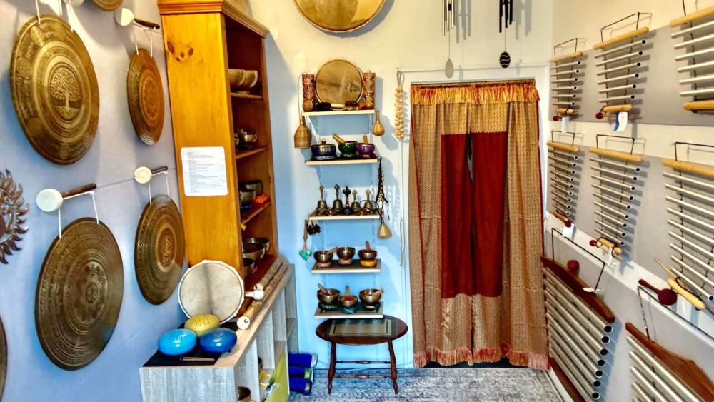 Sonora Studio sound healing space in Melbourne featuring gongs, singing bowls, and chimes displayed along the walls, with shelves of instruments and a warm, peaceful atmosphere.