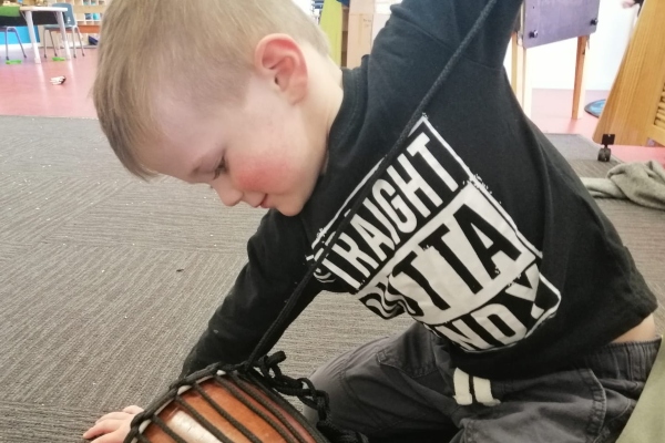 Child tightening rope on a small djembe during a drum making workshop for schools.