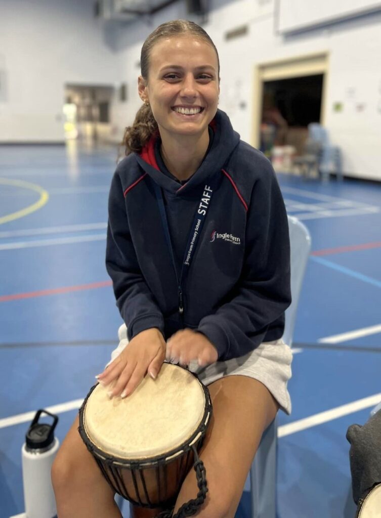 School staff member smiling while playing a djembe during a wellbeing drumming session.