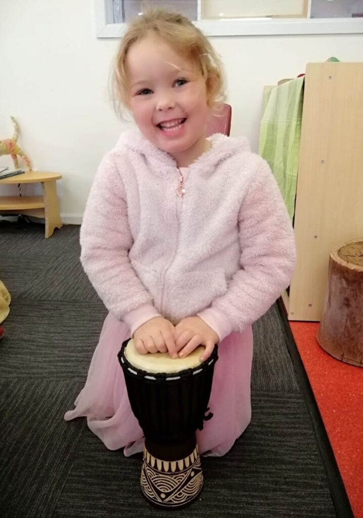 Young child smiling while working on a small djembe in a drum making workshop.