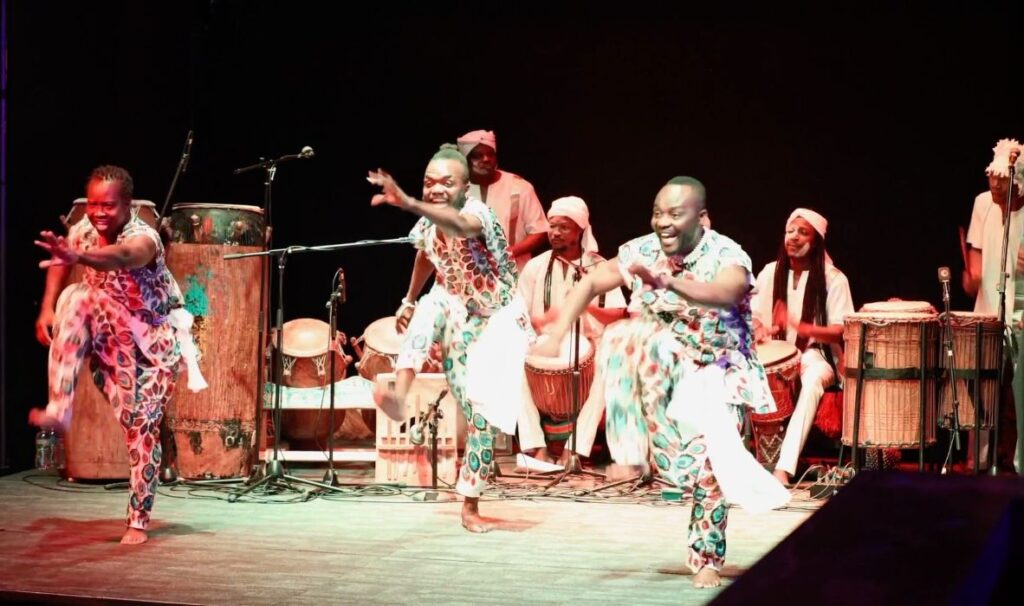 Members of the Wala band from Ghana standing behind traditional hand-carved West African drums during a live performance