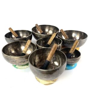 Seven-piece Tiger Eye chakra singing bowl set with wooden mallets, shown on coloured cushions