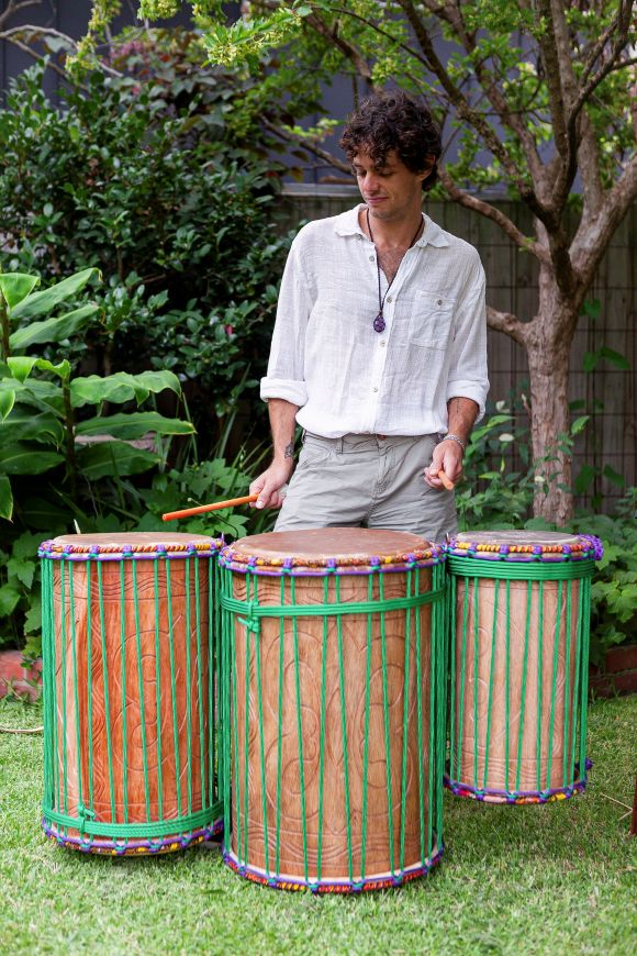 A full dunun set of three drums played upright with sticks, showing the carved hardwood shells and rope tuning